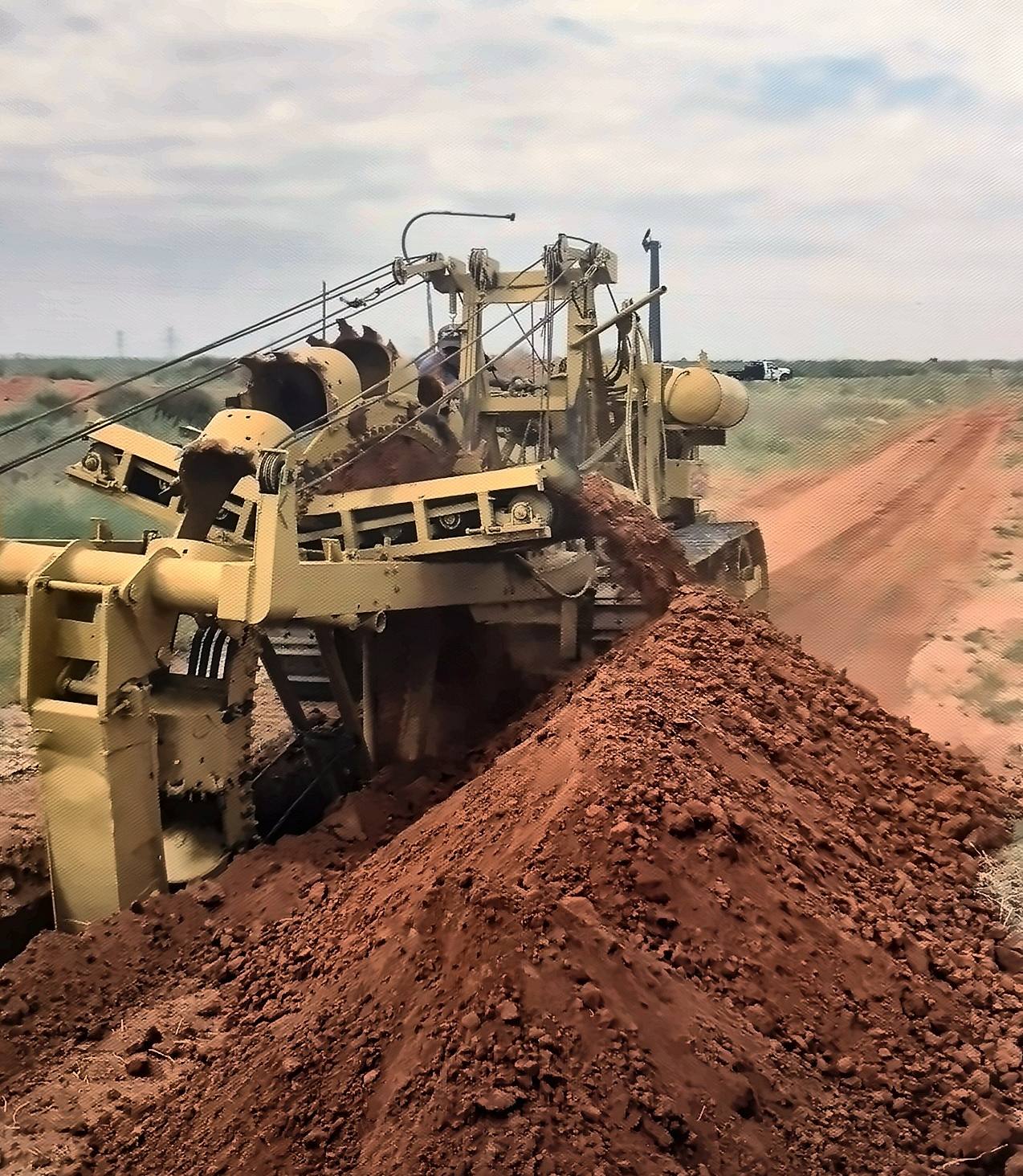 Wheel trencher piling red spoil beside a gathering line ditch