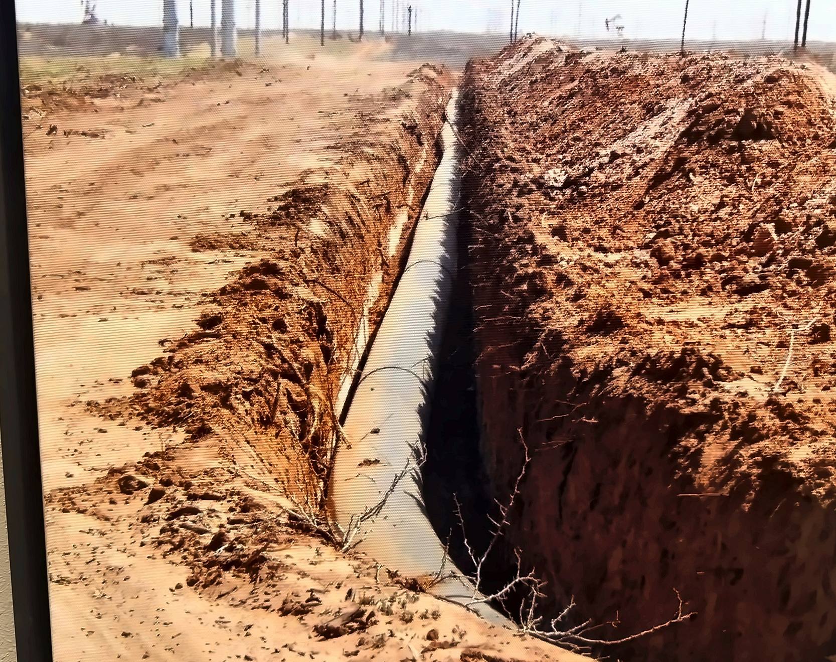 Coated steel pipeline running through an open trench toward the horizon