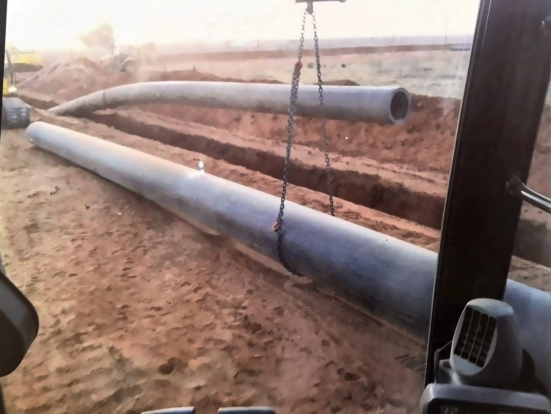 Large-diameter pipe strung along the right-of-way, seen from an equipment cab